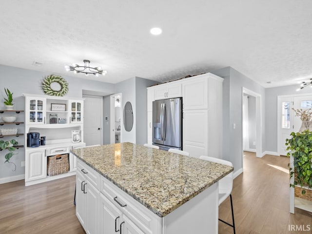 kitchen with stainless steel fridge with ice dispenser, a kitchen island, white cabinets, and light wood-type flooring