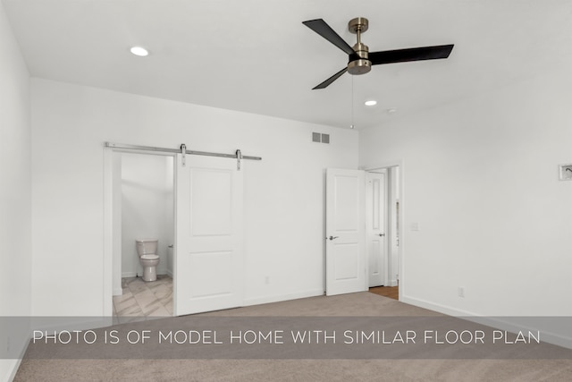 unfurnished bedroom with a barn door, ceiling fan, ensuite bath, and light colored carpet