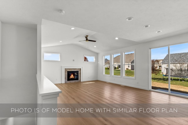 unfurnished living room featuring lofted ceiling, a stone fireplace, light hardwood / wood-style floors, and ceiling fan