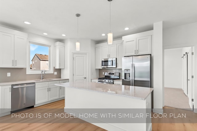 kitchen featuring stainless steel appliances, a kitchen island, sink, a barn door, and white cabinetry