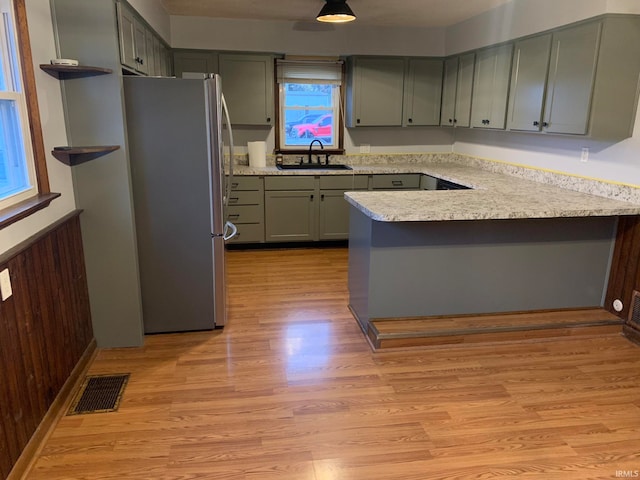 kitchen featuring kitchen peninsula, stainless steel fridge, sink, light hardwood / wood-style flooring, and wood walls