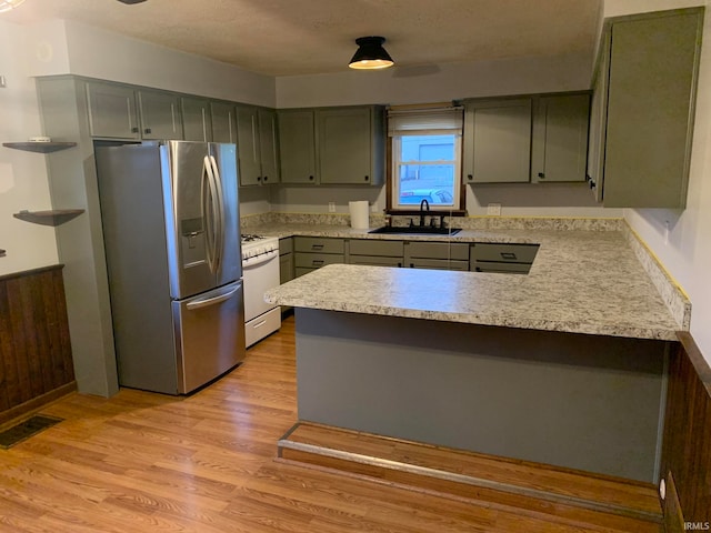 kitchen with kitchen peninsula, stainless steel fridge, gas range gas stove, sink, and light hardwood / wood-style floors