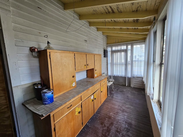 kitchen with tile countertops, a wealth of natural light, lofted ceiling with beams, and wood walls