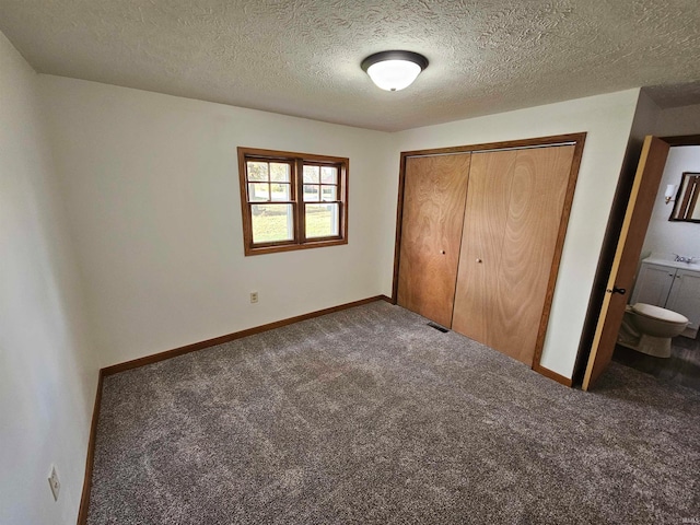 unfurnished bedroom with dark colored carpet, sink, ensuite bath, a textured ceiling, and a closet