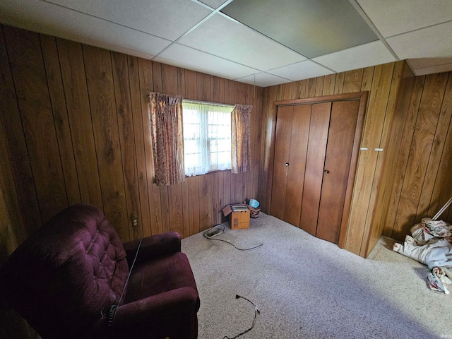 living area featuring a drop ceiling, carpet floors, and wooden walls