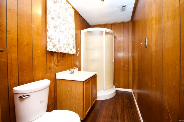 bathroom featuring hardwood / wood-style floors, toilet, wooden walls, vanity, and a shower with shower door