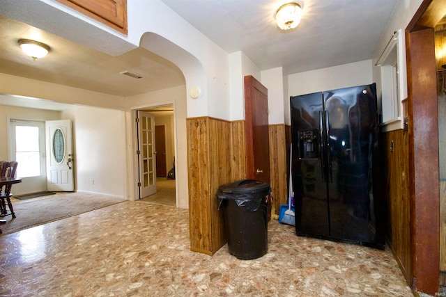 kitchen with wood walls, black fridge, and light carpet