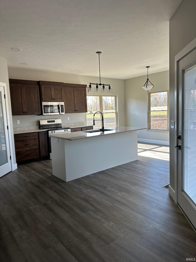 kitchen featuring dark brown cabinetry, sink, dark wood-type flooring, hanging light fixtures, and a kitchen island with sink