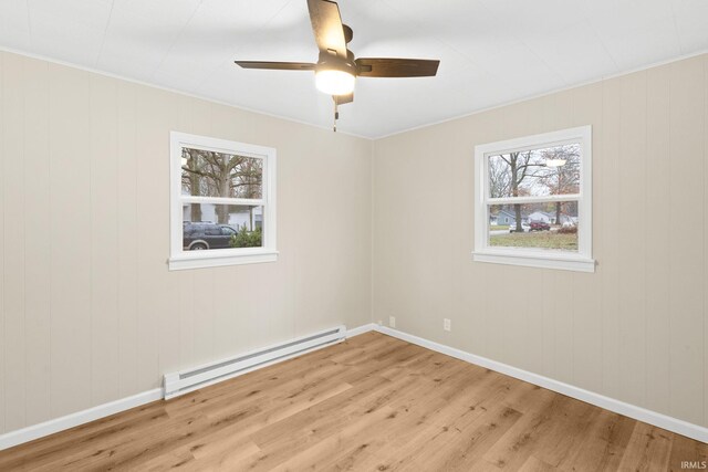 empty room with light wood-type flooring, a baseboard radiator, a wealth of natural light, and crown molding