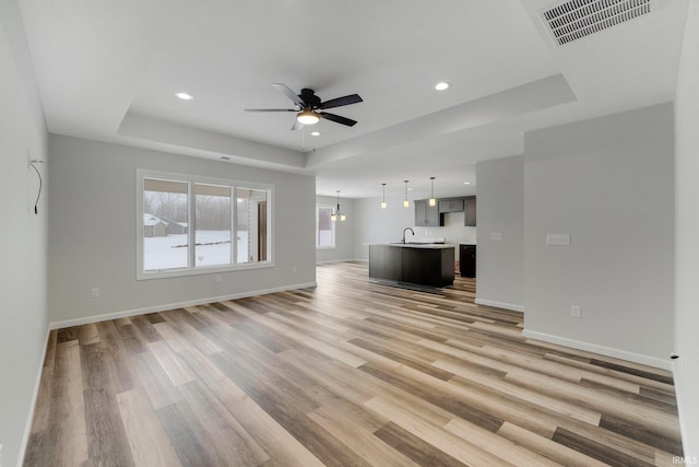 15384 Brimwillow Dr, Huntertown, IN 46748 - unfurnished living room featuring a raised ceiling, light wood finished floors, a ceiling fan, recessed lighting, and baseboards