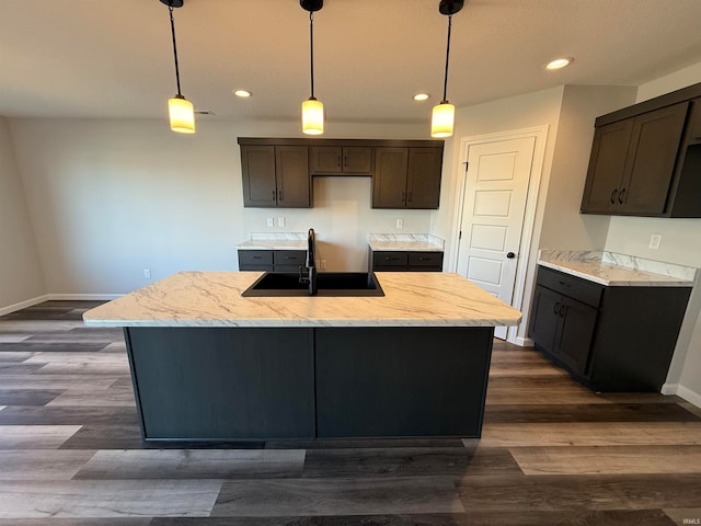 kitchen featuring sink, dark hardwood / wood-style flooring, decorative light fixtures, a kitchen island with sink, and dark brown cabinets