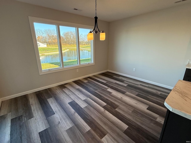 unfurnished dining area with a water view, dark wood-type flooring, and an inviting chandelier