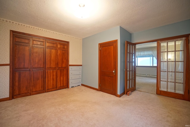 unfurnished bedroom with french doors, a textured ceiling, light colored carpet, baseboard heating, and a closet