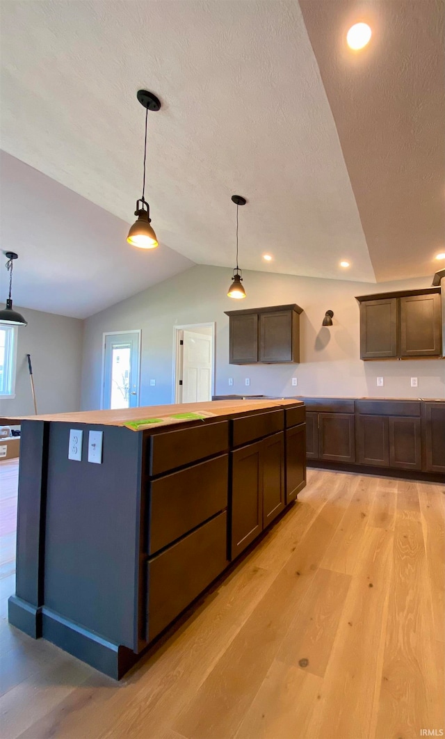 kitchen with dark brown cabinetry, light hardwood / wood-style flooring, pendant lighting, lofted ceiling, and a kitchen island