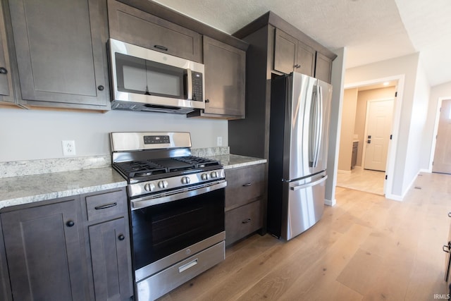 kitchen featuring dark brown cabinetry, light stone counters, stainless steel appliances, and light wood-type flooring