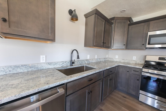 kitchen with sink, dark wood-type flooring, stainless steel appliances, light stone counters, and dark brown cabinets