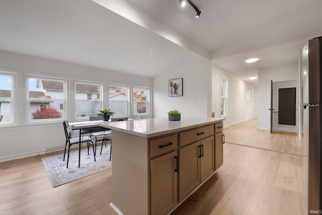 kitchen featuring light wood-type flooring, vaulted ceiling, a kitchen island, and stainless steel refrigerator