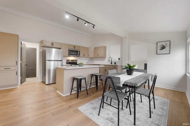 dining space featuring rail lighting, light hardwood / wood-style floors, lofted ceiling, and sink