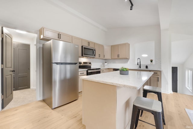 kitchen with a kitchen bar, appliances with stainless steel finishes, sink, light brown cabinets, and a kitchen island