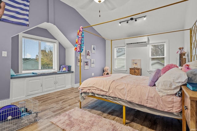 bedroom with lofted ceiling, light wood-style flooring, baseboards, an AC wall unit, and track lighting