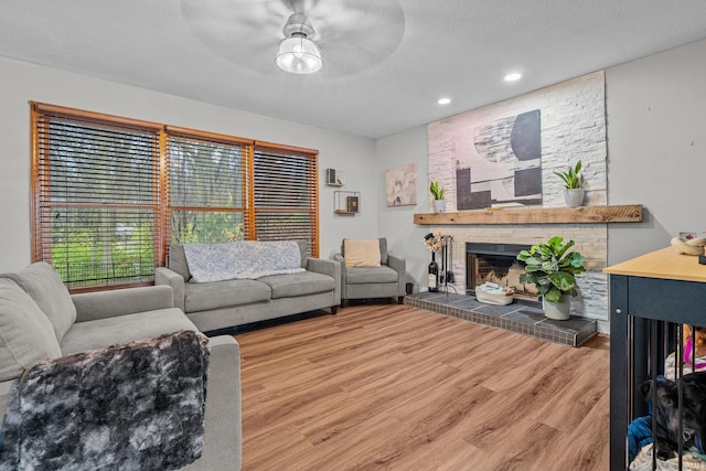 living room featuring hardwood / wood-style flooring, ceiling fan, a textured ceiling, and a brick fireplace