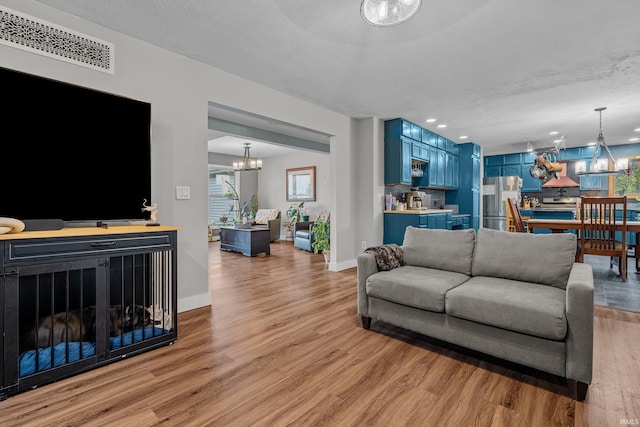 living area featuring a fireplace, visible vents, light wood-style flooring, an inviting chandelier, and baseboards