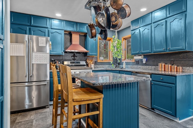 kitchen featuring appliances with stainless steel finishes, a center island, blue cabinets, custom exhaust hood, and a sink