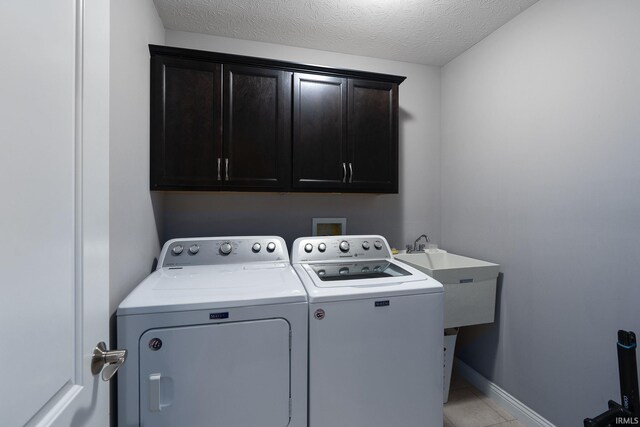 laundry room featuring washer and clothes dryer, cabinets, sink, light tile patterned floors, and a textured ceiling