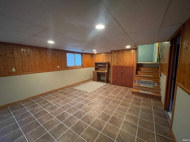 basement with a paneled ceiling, dark tile patterned floors, and wooden walls