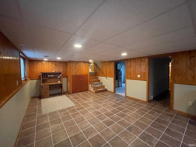 basement featuring a paneled ceiling, wood walls, and dark tile patterned floors