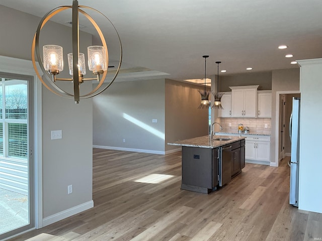 kitchen with white cabinetry, light stone counters, an inviting chandelier, and a center island with sink