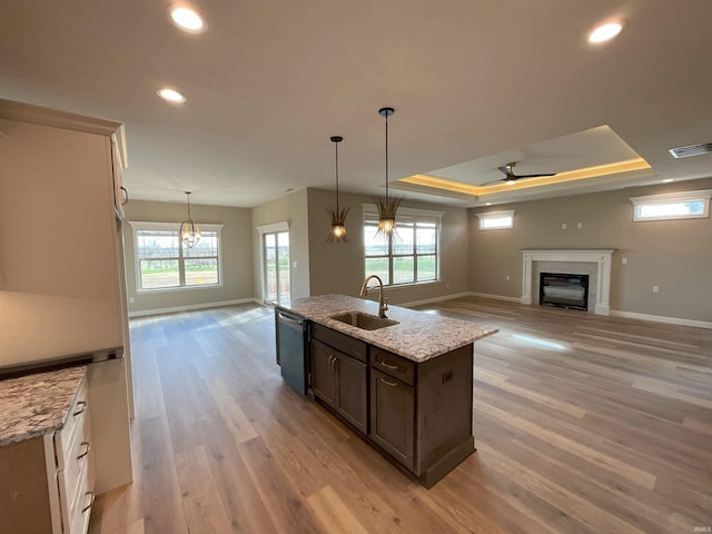 kitchen with dishwasher, sink, a raised ceiling, light stone countertops, and dark brown cabinets