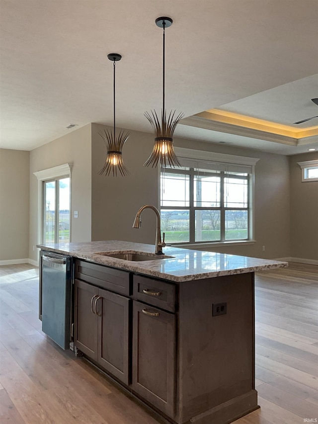 kitchen with sink, dishwasher, hanging light fixtures, a tray ceiling, and light stone countertops