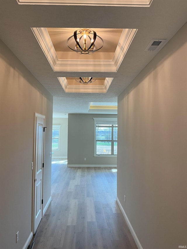 hall with a raised ceiling, ornamental molding, wood-type flooring, and a notable chandelier