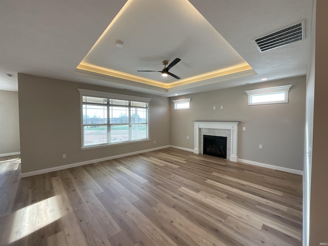 unfurnished living room featuring ceiling fan, a wealth of natural light, a raised ceiling, and light wood-type flooring