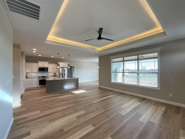 unfurnished living room featuring wood-type flooring, ceiling fan, and a tray ceiling