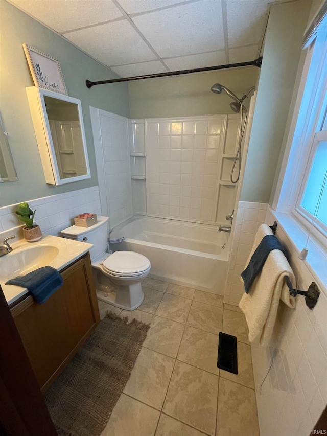 full bathroom featuring tile patterned floors, shower / bathtub combination, a drop ceiling, tile walls, and toilet