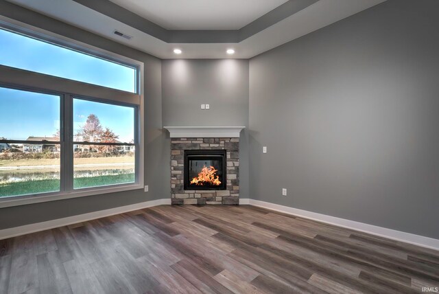 unfurnished living room with a fireplace, wood-type flooring, a water view, and a healthy amount of sunlight