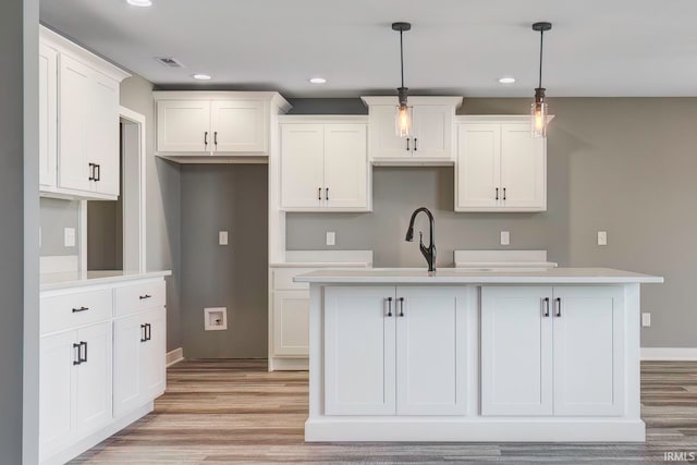 kitchen featuring white cabinetry, a kitchen island with sink, and hanging light fixtures