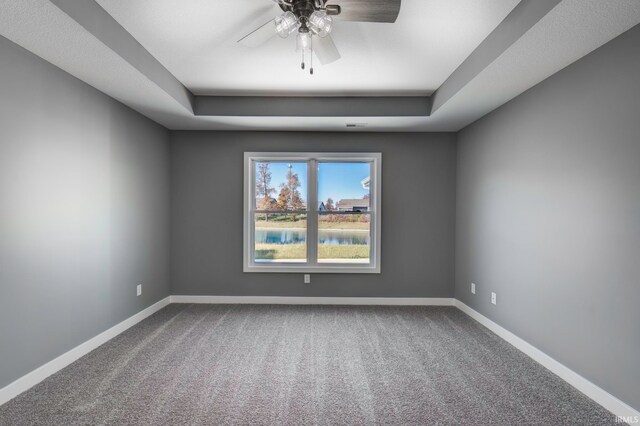 spare room with ceiling fan, a water view, carpet floors, and a tray ceiling