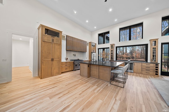 kitchen with stainless steel range, a towering ceiling, an island with sink, a breakfast bar area, and light wood-type flooring