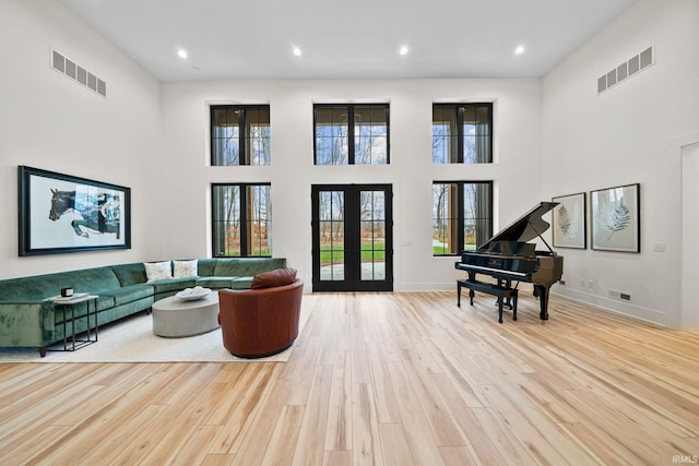 living room with a wealth of natural light, light hardwood / wood-style flooring, a high ceiling, and french doors