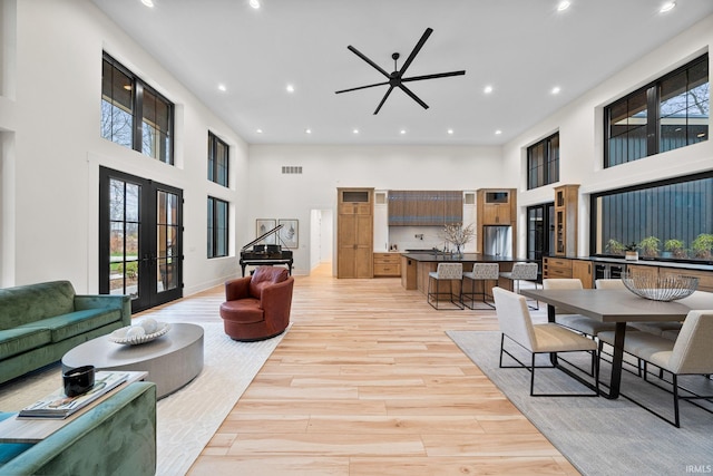 living room with ceiling fan, light wood-type flooring, a towering ceiling, and french doors