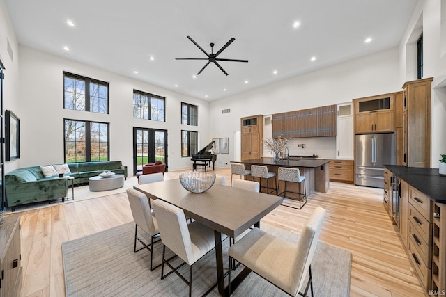 dining space featuring french doors, sink, ceiling fan, light wood-type flooring, and a towering ceiling