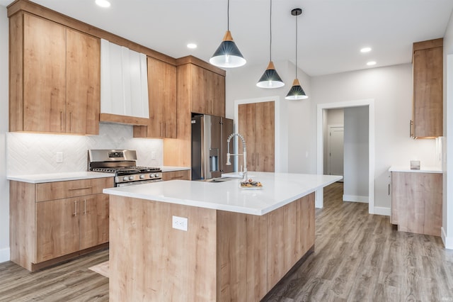 kitchen with sink, stainless steel appliances, decorative light fixtures, a center island with sink, and light wood-type flooring