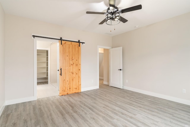 unfurnished bedroom with a spacious closet, ceiling fan, a barn door, light hardwood / wood-style flooring, and a closet