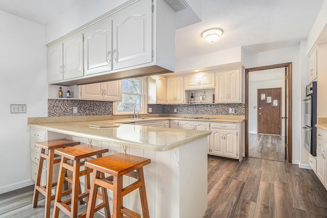 kitchen with kitchen peninsula, dark hardwood / wood-style flooring, a breakfast bar, sink, and white cabinets