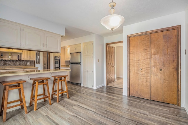 kitchen featuring a breakfast bar, kitchen peninsula, stainless steel refrigerator, and light hardwood / wood-style flooring