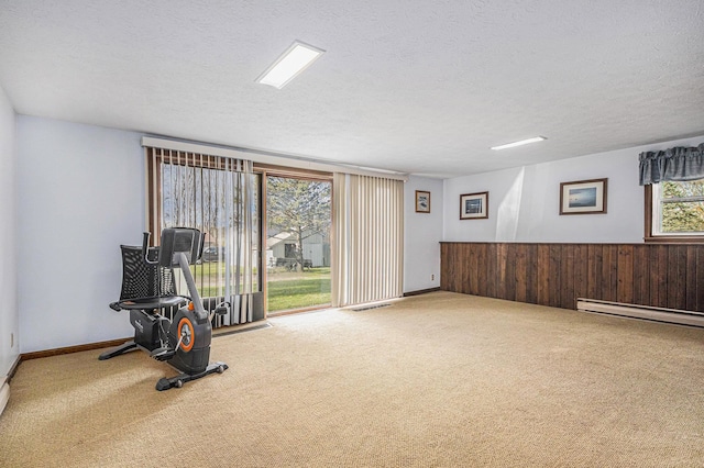 exercise room featuring wooden walls, carpet floors, a baseboard radiator, and a textured ceiling