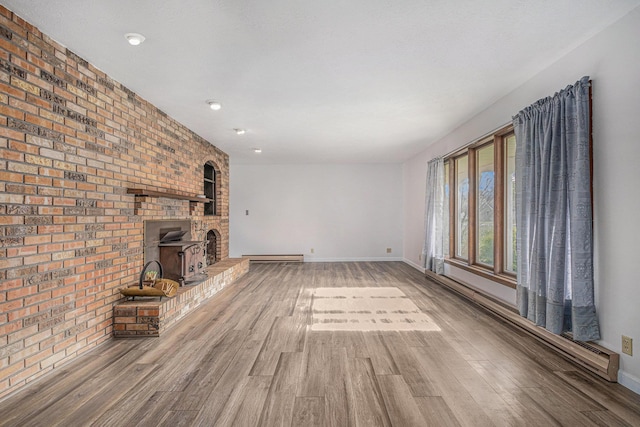 unfurnished living room with baseboard heating, a wood stove, hardwood / wood-style floors, and brick wall